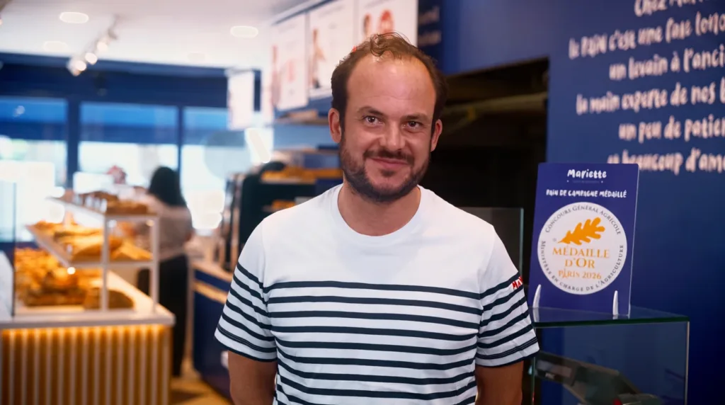 Amaury Cavé, franchisé Mariette à Bezons, souriant dans sa boutique devant le présentoir du pain de campagne médaillé d'or