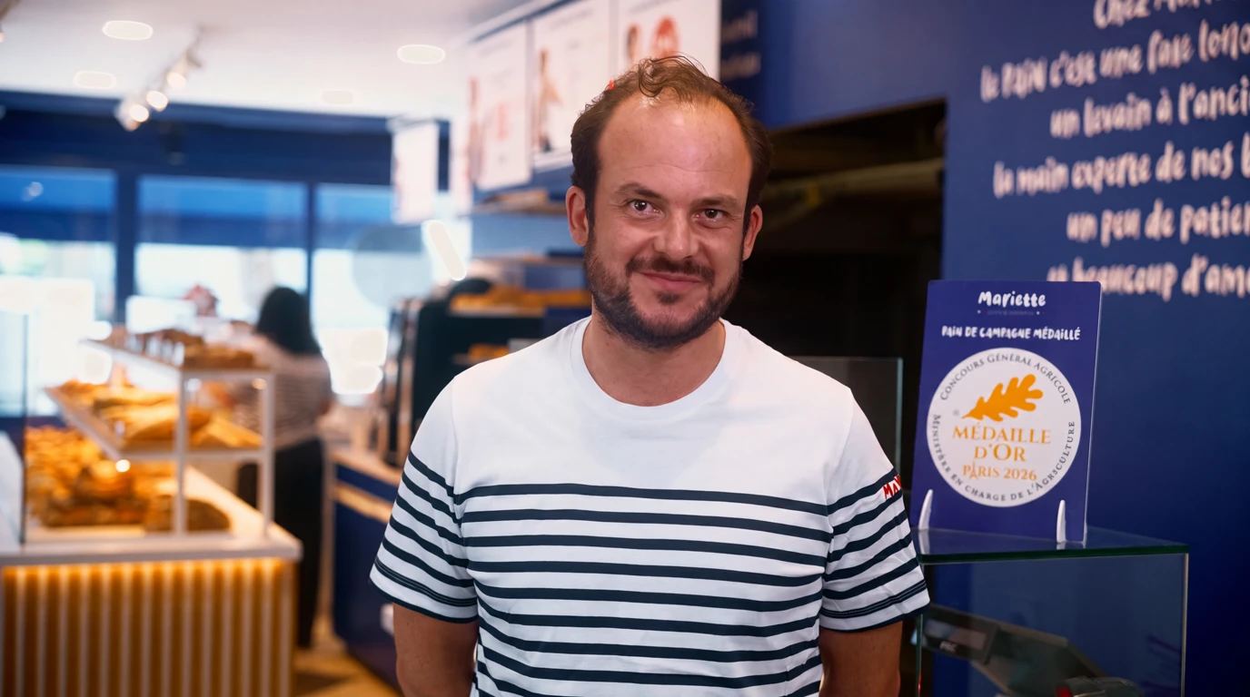 Amaury Cavé, franchisé Mariette à Bezons, souriant dans sa boutique devant le présentoir du pain de campagne médaillé d'or